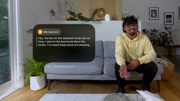 Links ist ein Text-Overlay mit Live-Untertiteln zu sehen, rechts sitzt ein Mann auf einem Sofa und spricht offenbar mit der Person, die das Bild betrachtet und die Untertitel sieht.